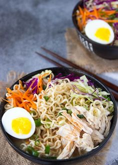 two bowls filled with noodles, meat and veggies next to chopsticks