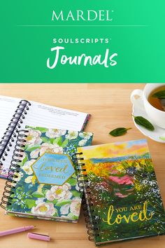 two notebooks sitting on top of a wooden table next to a cup of tea