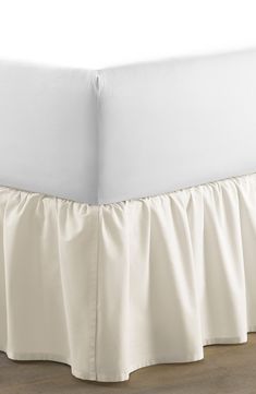 white bed skirt with ruffles on the bottom and bottom edge, in front of a wooden floor