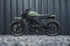 a green motorcycle parked in front of a metal wall with gravel on the ground next to it