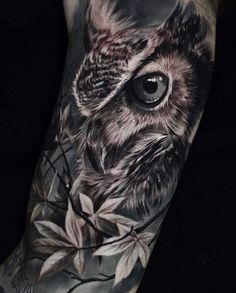 an owl tattoo on the arm with leaves and branches around it's eyes is shown