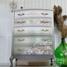 an old dresser has been painted silver and gold with floral designs on the drawers, as well as a green vase