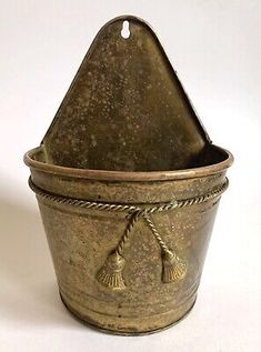 an old metal bucket with tassels on the handles and bottom, sitting on a white surface