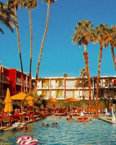 people swimming in a pool surrounded by palm trees and lounge chairs with yellow umbrellas