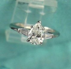 an engagement ring with three pear shaped diamonds on it's side, in front of a clear box