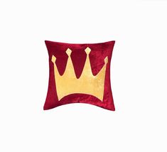 a red and gold pillow with two crowns on it's side, against a white background