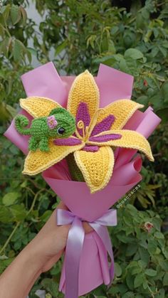 a hand holding a crocheted flower with a green frog on it's back