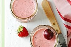 two jars filled with pink smoothie next to a strawberry