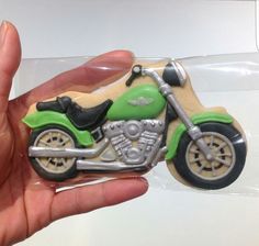 a hand is holding a cookie shaped like a motorcycle with green and white paint on it