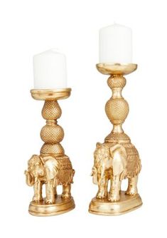 two golden candlesticks with white candles on them and an elephant figurine