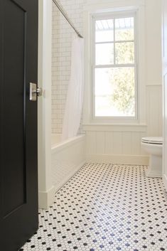 a bathroom with black and white tile flooring next to a window in the wall