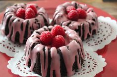 three small cakes with raspberries on top of each one sitting on a red plate