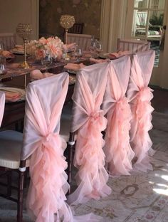 a dining room table with chairs covered in pink chiffon sashes and place settings