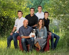 a group of people sitting on top of a red chair in the grass with a dog