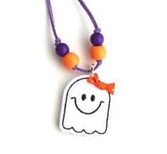 a necklace with an orange bow and a white ghost on it's head is hanging from a purple cord