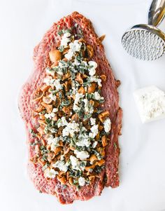 a piece of meat covered in various toppings next to a grater and spoon