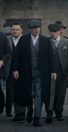 a group of men walking down a street next to each other in suits and hats