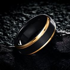 a black and gold wedding ring sitting on top of a rocky surface in the dark