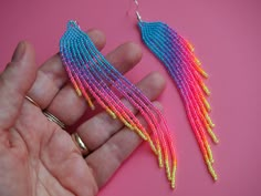 a pair of colorful beaded earrings being held by someone's hand on a pink surface