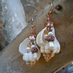 two seashells with pearls and copper wire hang from earwires on a piece of wood