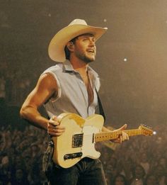 a man wearing a cowboy hat playing an electric guitar in front of a large crowd