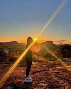 a person standing on top of a dirt field with the sun setting in the background