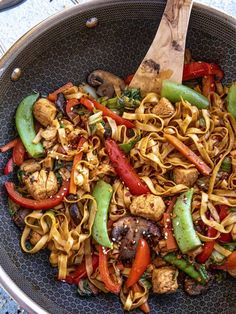 a pan filled with noodles and vegetables on top of a table next to a wooden spoon