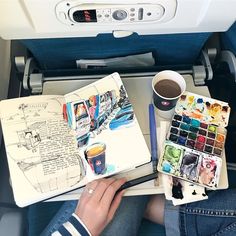 a person sitting in an airplane holding a cup of coffee and writing on a notebook