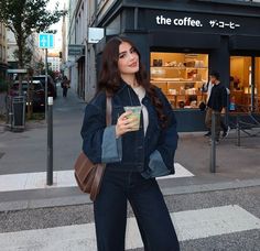 a woman standing in front of a coffee shop holding a cup and looking at the camera