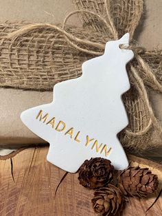 a white ceramic ornament with the word madam on it next to two pine cones