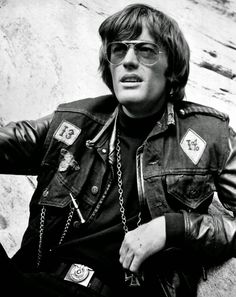 a man sitting on the ground wearing sunglasses and a leather jacket with chains around his neck