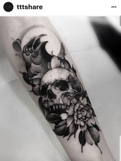 a black and white photo of a skull with flowers on it's arm,