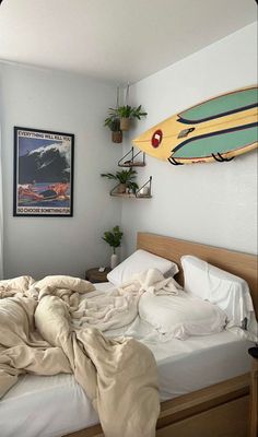 an unmade bed with a surfboard on the wall above it in a bedroom