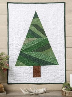 a quilted christmas tree hanging on the side of a wall next to a potted plant