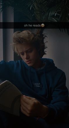 a young man reading a book in front of a window with the caption oh he reads