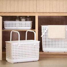 two white baskets sitting next to each other on top of a wooden shelf in front of a cabinet