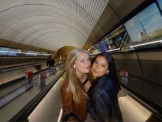 two beautiful young women standing next to each other on an escalator in a subway station