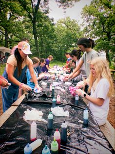 a group of people standing around a table covered in plastic bottles and containers filled with liquid