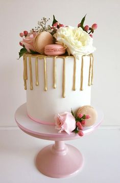 a white and gold cake with macaroons, roses and macaroons on top