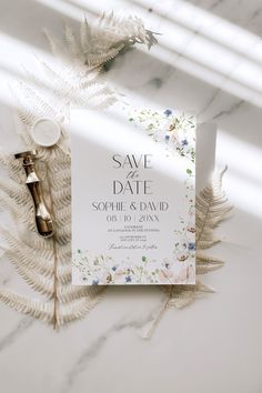 an elegant save the date card on top of a white marble table with feathers and flowers