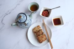 two plates with food and chopsticks next to a teapot on a table