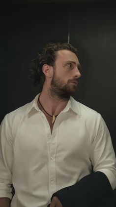 a man with long hair and beard wearing a white shirt looking off into the distance