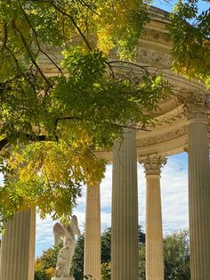 an old building with columns and statues on the sides, surrounded by trees in front of it