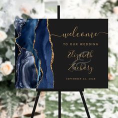 a black and gold wedding welcome sign on a easel with flowers in the background