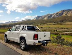 a white pick up truck parked on the side of a road in front of mountains