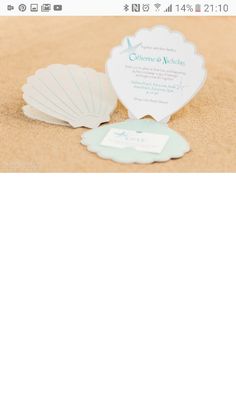 the wedding card is laying on the sand and it has shells in front of it