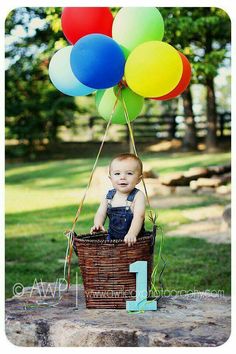 a baby sitting in a basket with balloons attached to the handle and number one on it