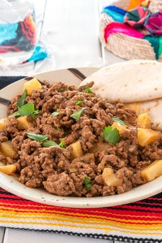 a white plate topped with meat and potatoes next to a tortilla on top of a table