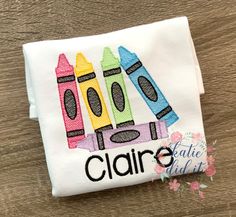 a white shirt with crayons on it and the words claire written in black