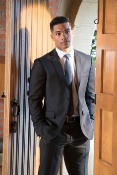 a man wearing a suit and tie standing in front of a door with his hands in his pockets